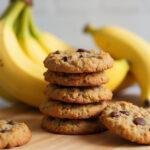 Cookies banane healthy sans sucre présentés sur une planche en bois avec des bananes fraîches, parfaits pour une collation saine.