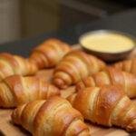 Croissants au jambon fromage feuilletés maison, dorés et feuilletés, présentés sur une planche à découper dans une cuisine chaleureuse.