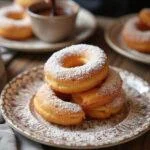 Assiette élégante de Crullers Français dorés avec du sucre glace, prête à être dégustée avec une sauce au chocolat.