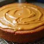 Gâteau au beurre de cacahuète, doré et arrosé de beurre de cacahuète fondu, exposé sur une grille.