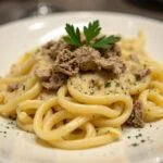 Présentation des pâtes crémeuses à la truffe noire sur une assiette avec une garniture élégante.