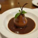 Dessert final de Recette Poire Belle-Hélène au Chocolat présenté sur une table, avec des poires pochées, une sauce au chocolat riche et une feuille de menthe.