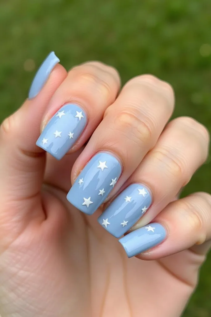 Gros plan sur une main avec un vernis bleu clair brillant et décorations d'étoiles, illustrant une manucure chic et adorable.