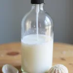 Une bouteille en verre contenant une brume capillaire maison au sel de mer sur une surface en bois, accompagnée d'accessoires de plage