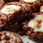 A close-up of a freshly baked Brown Butter Brookie cut into squares, displaying a marbled swirl of chocolate and cookie dough with a shiny golden brown crust on top, placed on a rustic wooden surface with a few scattered chocolate chips and a drizzle of caramel.