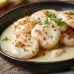 Une assiette de coquillettes garnie de morceaux de bœuf tendre, nappée d'une sauce crémeuse, avec du fromage fondu sur le dessus, présentée dans une vaisselle blanche élégante.