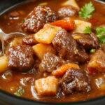 A steaming bowl of hearty beef stew featuring tender chunks of beef, orange carrots, and potatoes immersed in a rich, thick gravy, garnished with fresh herbs, served on a rustic wooden table with a side of crusty bread.