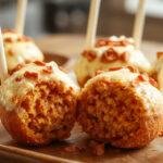 A close-up of several round pumpkin cake pops coated in vibrant orange and white drizzle, displayed on a rustic wooden surface with scattered fall leaves around, highlighting their smooth texture and festive presentation.