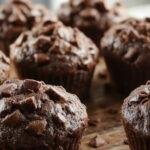 A close-up of a freshly baked chocolate pumpkin muffin topped with a drizzle of chocolate glaze, nestled on a rustic wooden plate with a few pumpkin seeds scattered around, golden-brown crust contrasting with the dark chocolate streaks.