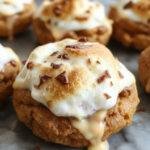 A close-up of Pumpkin S'mores Cookies showcasing golden-brown edges topped with melted marshmallow and a drizzle of chocolate, with a pumpkin spice sprinkle on top. The cookies are layered with marshmallow and chocolate, with some gooey marshmallow slightly oozing out, all presented on a rustic wooden platter.
