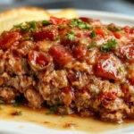 A close-up of a hearty and moist meatloaf sliced to reveal a tender, juicy interior. The meatloaf is topped with a glossy tomato glaze, garnished with fresh herbs, and served on a rustic white plate next to a side of mashed potatoes and green beans. The presentation emphasizes the moist texture and rich flavor, with steam gently rising from the hot dish.