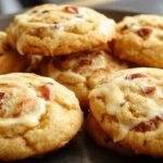 A plate of golden-brown Butterbeer cookies with cracks on top, sprinkled with a light dusting of cinnamon, presented on a rustic wooden table with a Hogwarts-themed backdrop, soft natural lighting highlighting their chewy texture and inviting appearance.