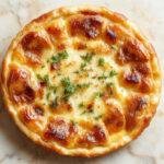 Une quiche Lorraine traditionnelle dans une tarte en pâte brisée, garnie de lardons dorés, d'œufs et de crème, décorée d'un léger brunissement à la surface et présentée sur une planche en bois, prête à être servie.