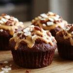 A close-up of two luscious salted caramel chocolate cupcakes on a rustic wooden surface. The cupcakes have a rich, glossy chocolate top decorated with a drizzle of golden salted caramel sauce and a sprinkle of sea salt crystals. The surrounding area features a few caramel swirls and cocoa powder dusted lightly around the cupcakes, creating a tempting and inviting scene.