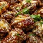 Golden-brown beef bites coated in glossy garlic butter sauce, arranged on a white plate with fresh herbs and roasted garlic cloves, steam rising subtly