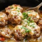 A close-up of tender, golden-brown Salisbury steak meatballs arranged in a rustic bowl, topped with a rich, glossy gravy and garnished with fresh herbs. The dish is plated on a parchment-lined surface with a side of creamy mashed potatoes and steamed vegetables in the background, evoking a warm and comforting homestyle meal.