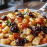 A vibrant Halloween pasta salad featuring brightly colored spiral pasta, orange and black olives, cherry tomatoes, and green herbs arranged in a festive bowl, with spooky-themed decorations around the plate.