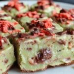 A rectangular plate of dark chocolate vampire fudge topped with bright red cherry syrup to resemble blood, garnished with small white marshmallows resembling vampire teeth, with a Halloween-themed background including pumpkins and black fabric.