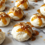 A close-up of small round goat cheese bites topped with golden honey and fresh herbs, arranged neatly on a white ceramic plate with a soft focus background. The bites are creamy with a slightly crumbly texture, drizzled with glossy honey that glistens under natural light, styled with delicate herbs for a fresh touch.